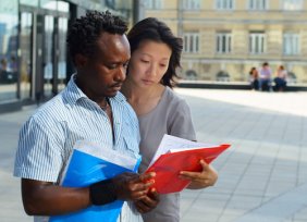 Man and woman with folders of information, urban campus buildings in backgroun