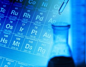 A blue periodic table with a drop of liquid being put into a flask
